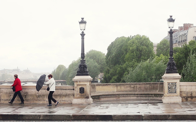 Deux personnes marchent sur un pont parisien sous la pluie.