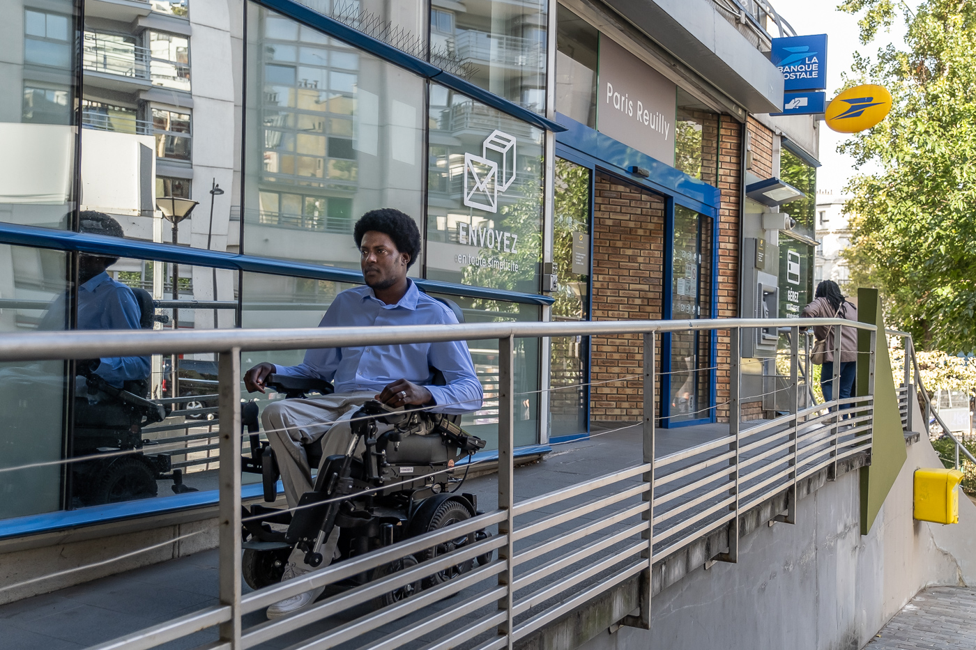 Personne en fauteuil roulant électrique devant une Poste