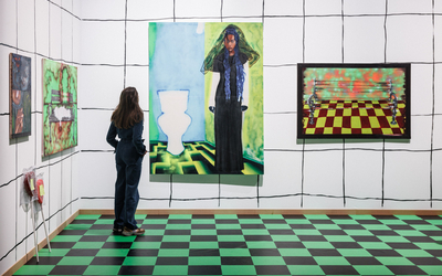 Une femme regarde des toiles colorés accrochées au mur 