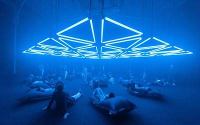 Un groupe de personnes assis sur des coussins dans une salle éclairée par des installations lumineuses bleues 